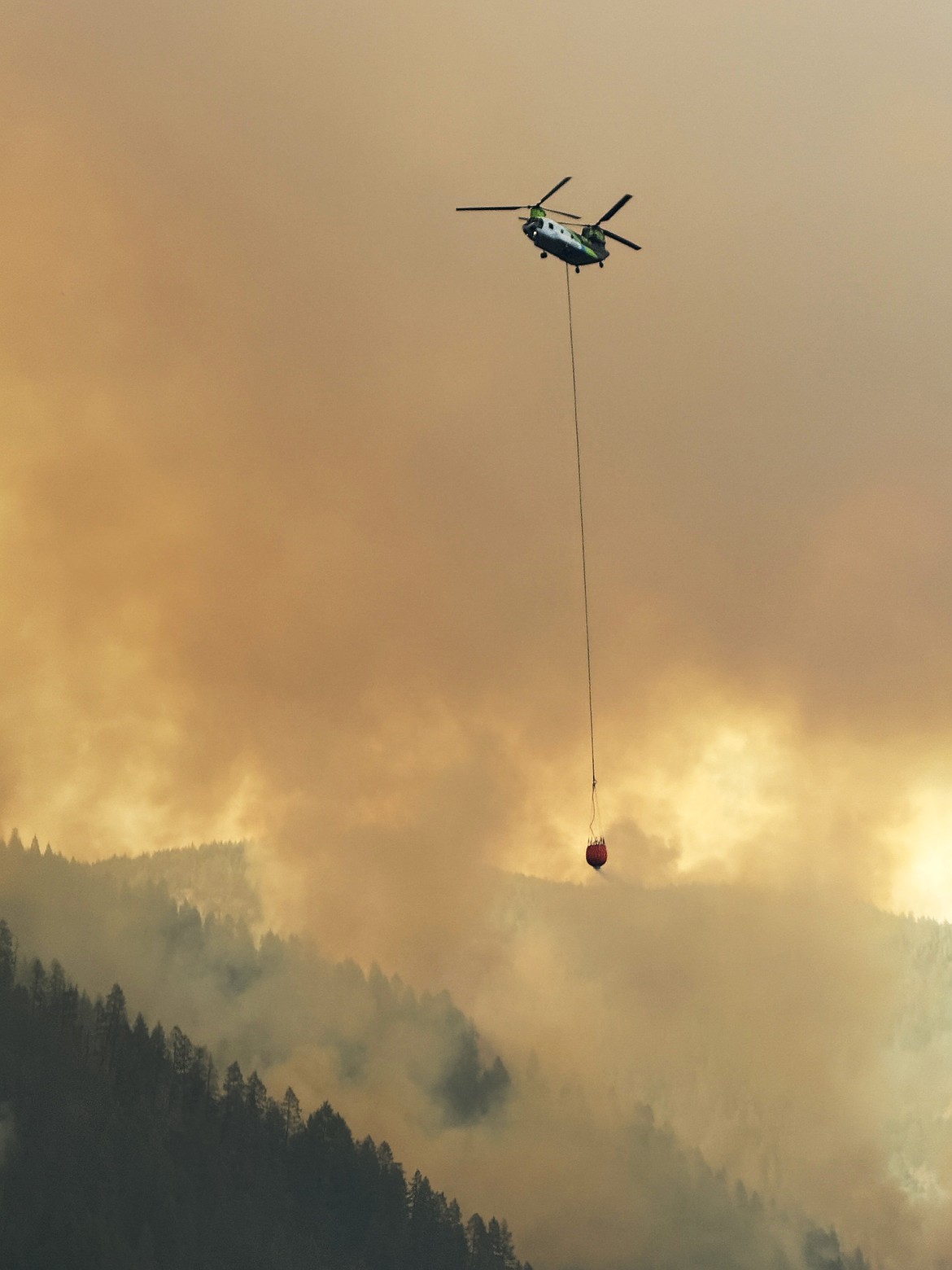 A helicopter is seen silhouetted against the smoke as it readies to drop a lot of water on the Sunset Fire on Thursday, Aug. 14.