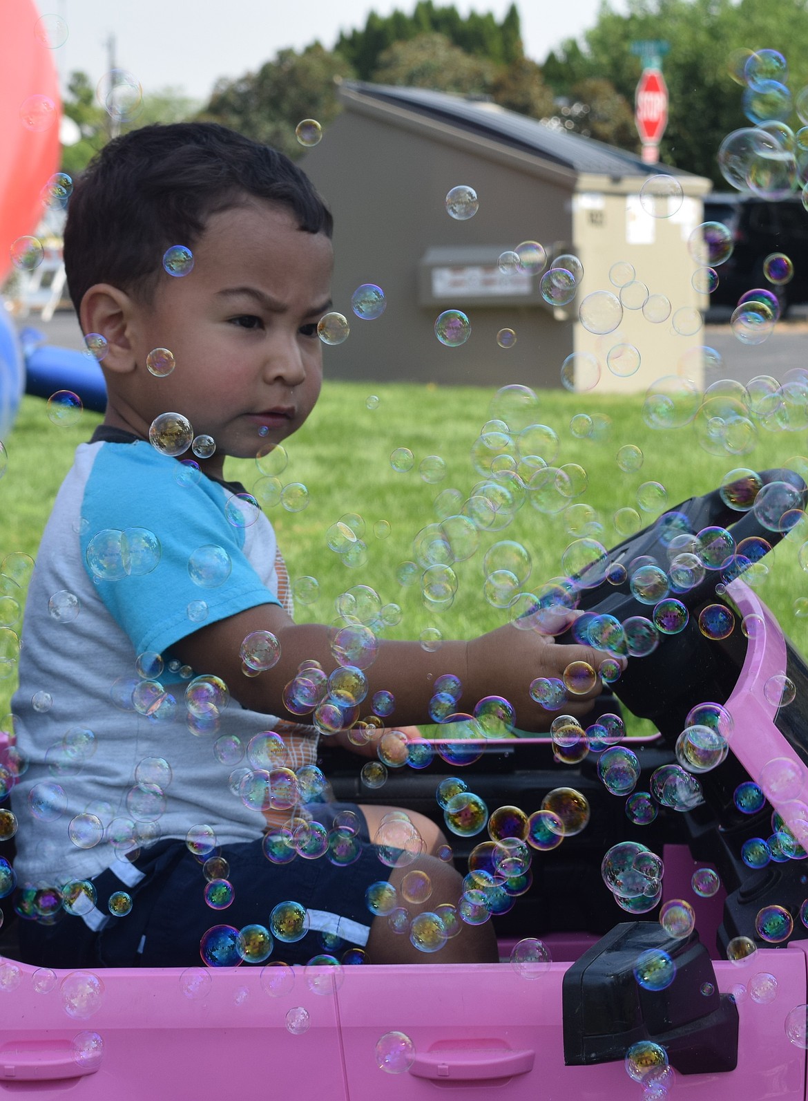 A young Warden community member has bubbles blown at him as he sits in his pink car.