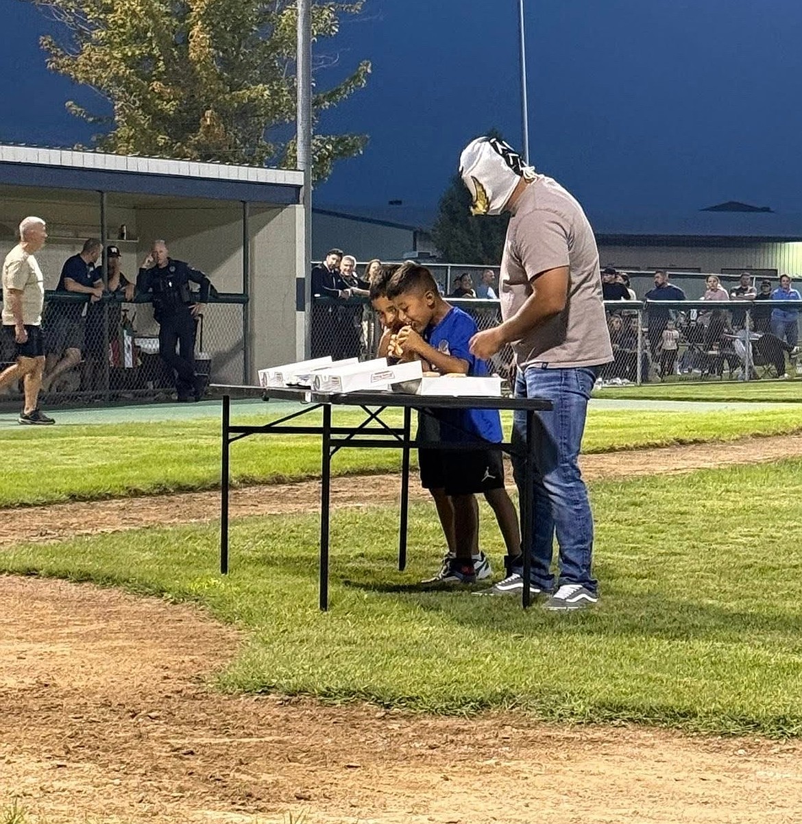 Two boys compete in a donut eating contest alongside Lucha Libre Shadow Night. The softball event raised funds for the Safe Streets project to raise gang awareness and diversion.