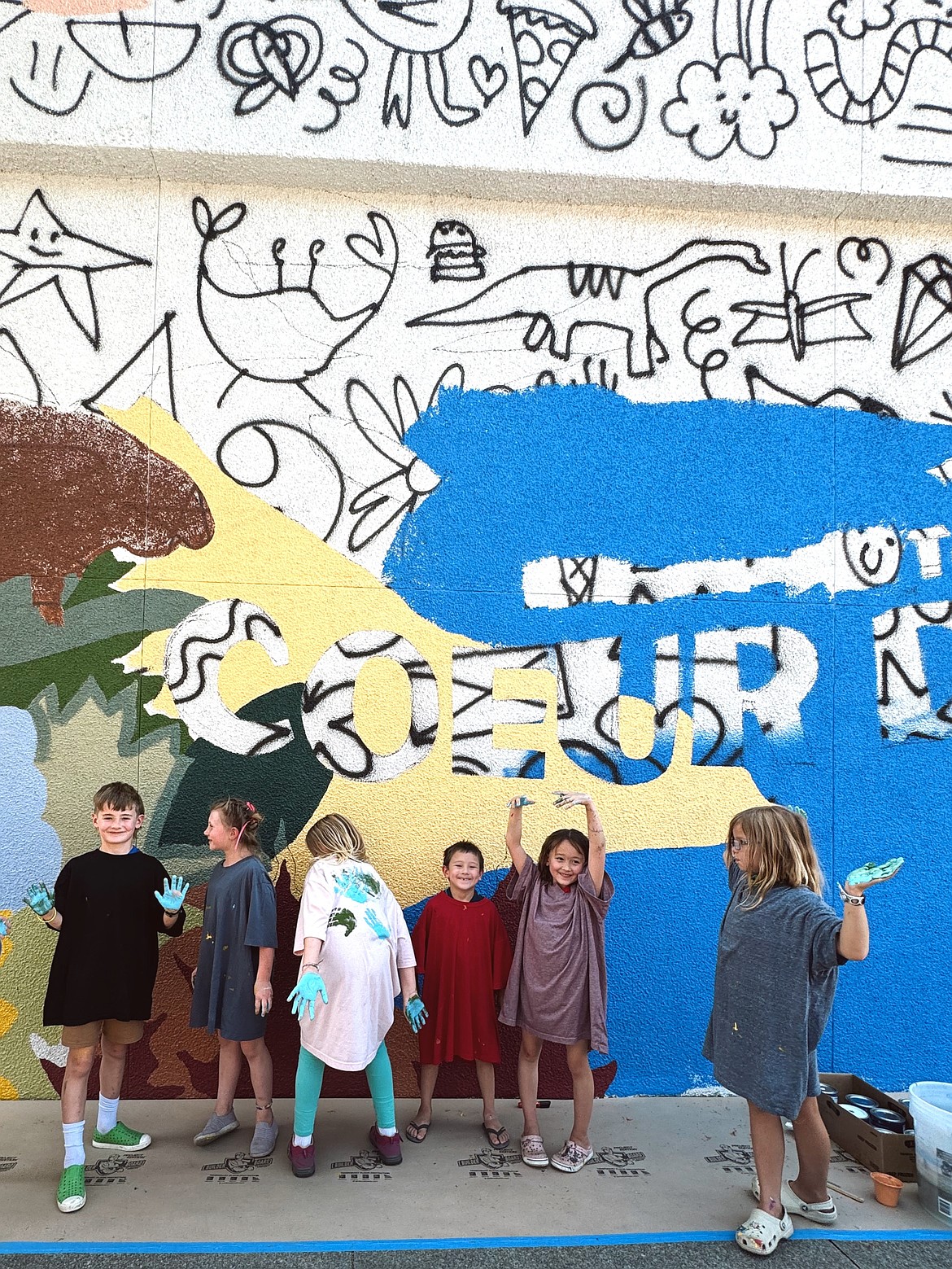 Kids participating in Emerge CDA's summer programs show off their colorful hands after adding their own touches to Gabrielle Lewis's new mural in downtown Coeur d'Alene.