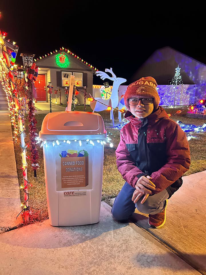 Weston Wesselman of Moses Lake kneels beside the food donation bin he set up outside his family’s Christmas light display.