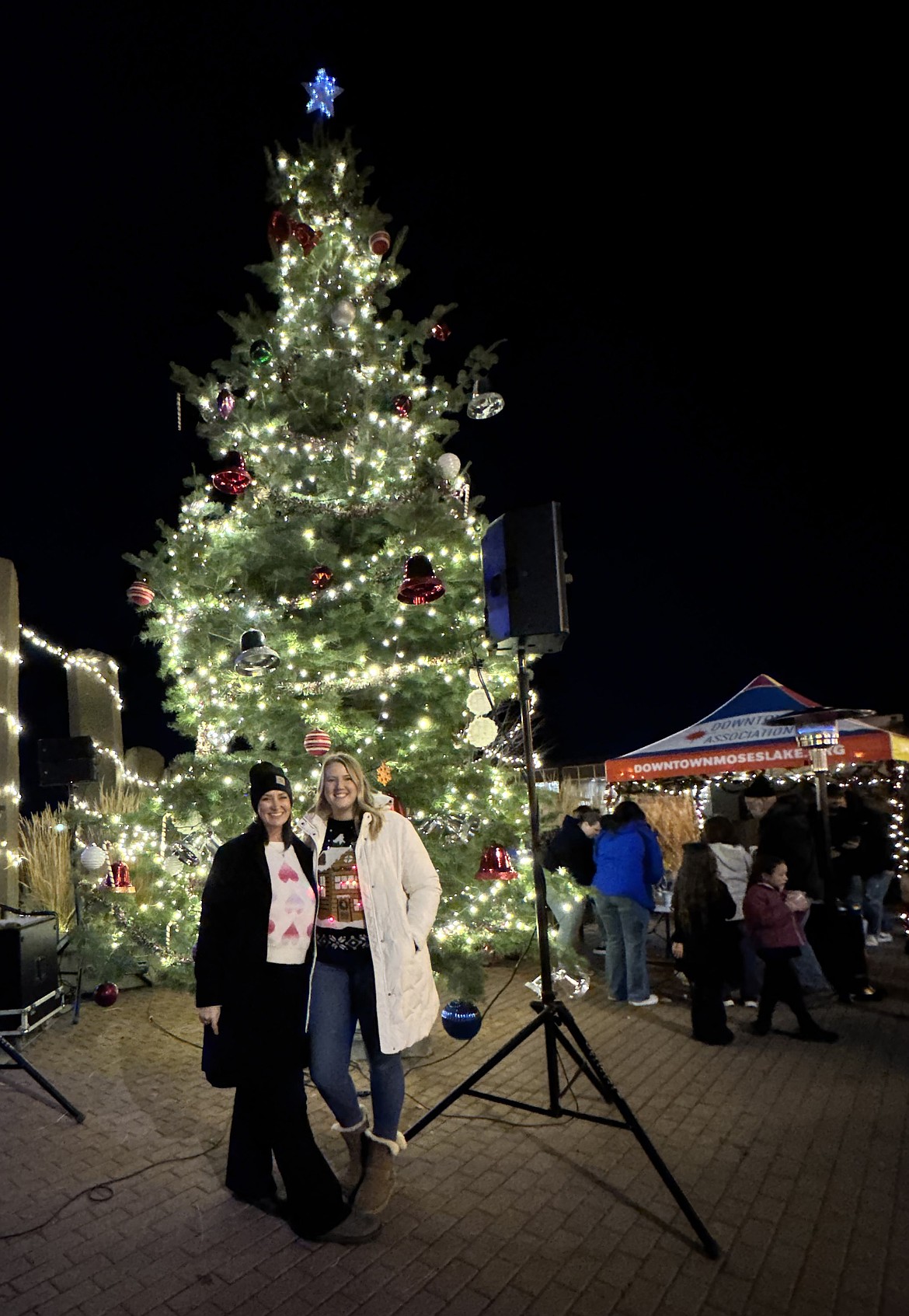 Downtown Moses Lake Association President Denise Kinder, left, and Director Mallory Miller stand in front of the big tree at last year’s Downtown Tree Lighting. This year’s event is Friday.