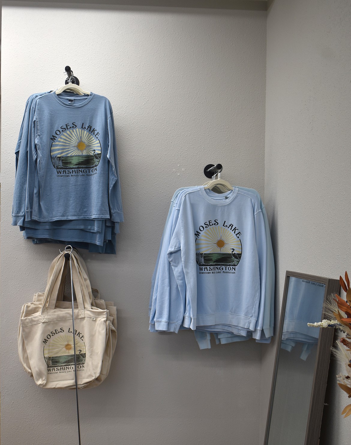 Moses Lake-themed shirts, hoodies and tote bags hang in the Downtown Moses Lake Associaiton’s office on South Division Street.