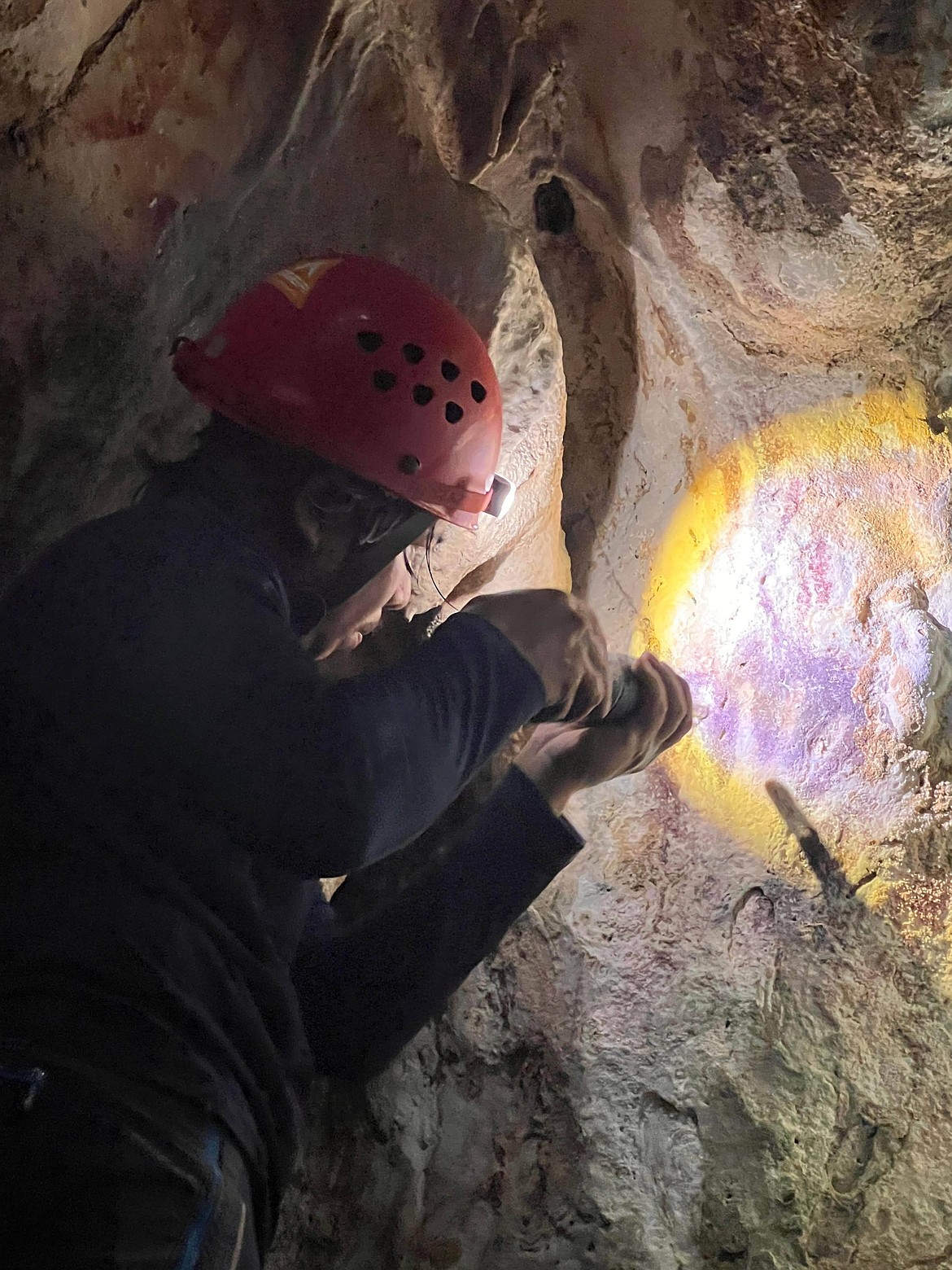 This image provided by Maxime Aubert shows scientist Adhi Agus Oktaviana studying handprints on the walls of a cave in Sulawesi, Indonesia.