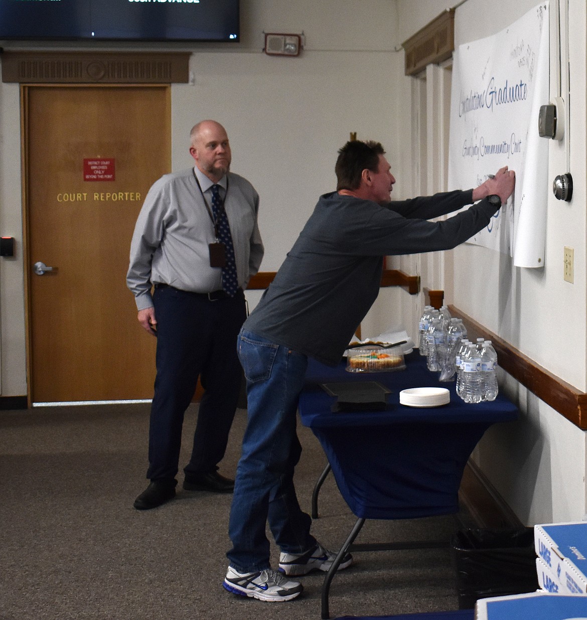 Shannon Robinson signs the banner alongside the names of the previous 15 Community Court graduates as Judge Brian Guinn looks on.