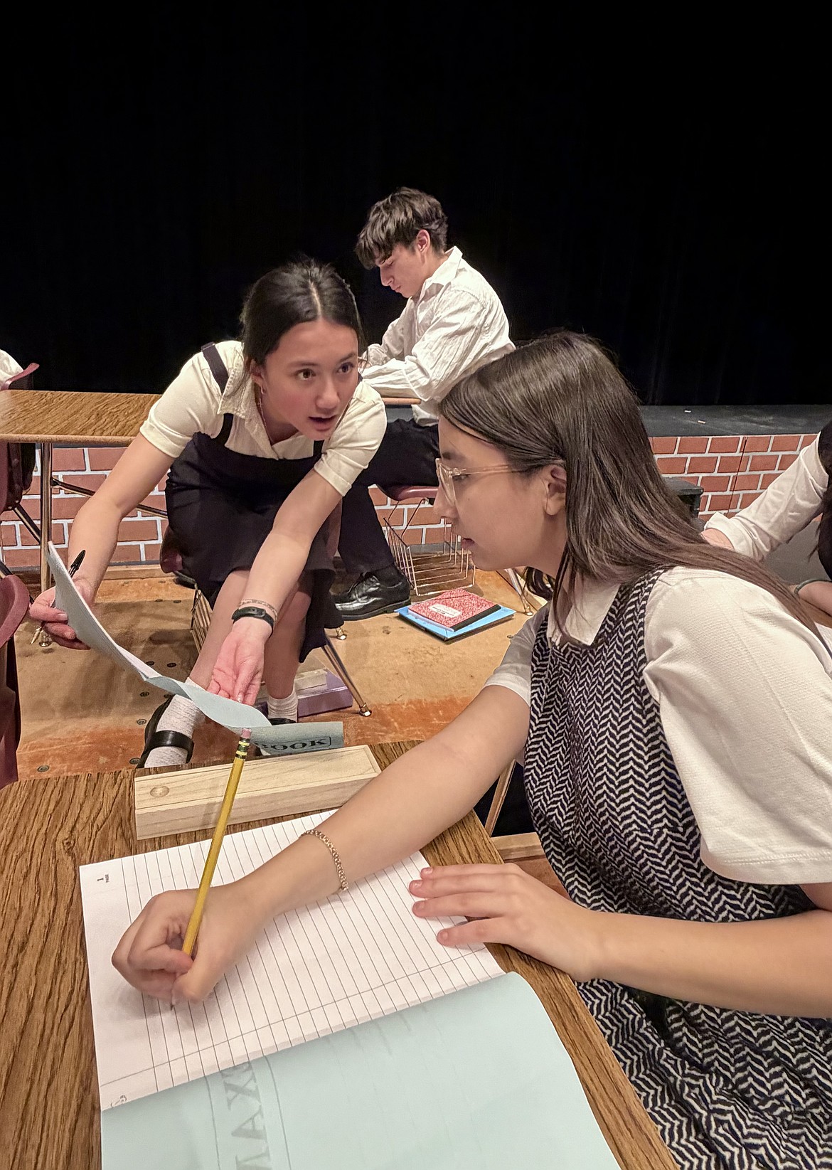 During one scene, the 1960s students are asked to take their annual exam, with several students turning to their peers for assistance. Rachel Gordon (Madeline Beck), left, leans over to ask a question and Carole Blanca (Jazelle Gonzalez), right, begins to look for the answer.
