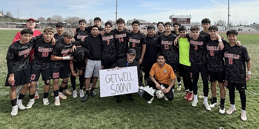 Huskies Head Soccer Coach Bernie Garza sits with the Huskies soccer team before last Saturday’s game while holding up a “Get Well Soon” poster that the team created for him.