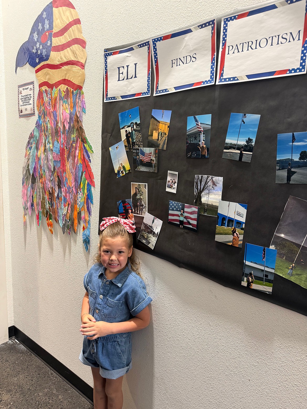 Five-year-old Revie Allen stands in front of a collage AIM School students made of photos taken in front of American flags with their stuffed companion Eli the Eagle.