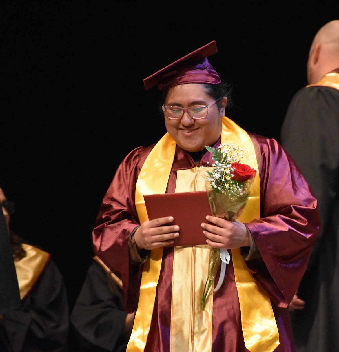 During the MLHS Pals graduation, Iris Lagunas stands on stage with a smile on her face and her diploma and a rose in hand.