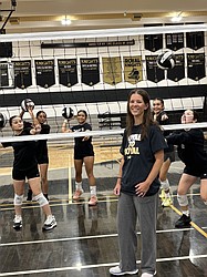 Melanie Griffin, the new head coach for the Royal Knights Volleyball team stands in front of the net with the team’s returning players in the background.