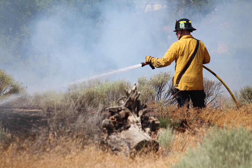 A  Moses Lake Fire Department firefighter sprays water on a fire along the lakeshore near North Fig Street Monday.