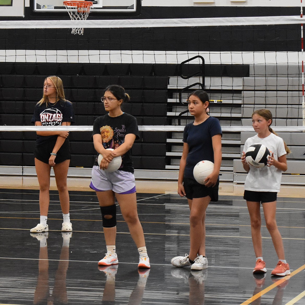 Emilie Lira stands alongside two youth volleyball players with Avery Scroggins on the other side of the net as the group gets ready to participate in an exercise.