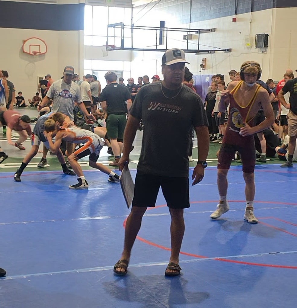Mavs Head Coach Jose Tanguma keeps an eye on things on the mat with Owen Martel following behind him in the background.