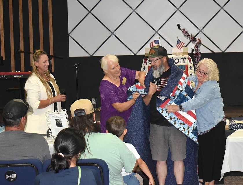 Kathy Aldrich, left, and Karrie Roberts wrap veteran Martin Flick in a Quilt of Valor Monday as Soap Lake Freedom Quilts of Valor leader Jenn Tincher, far left, looks on.