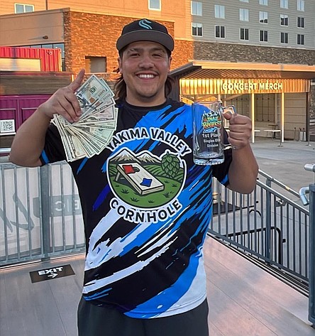 Camryn Barrientoz holds up prize money and a first place mug after a successful day at the PNW Bagfest cornhole tournament.