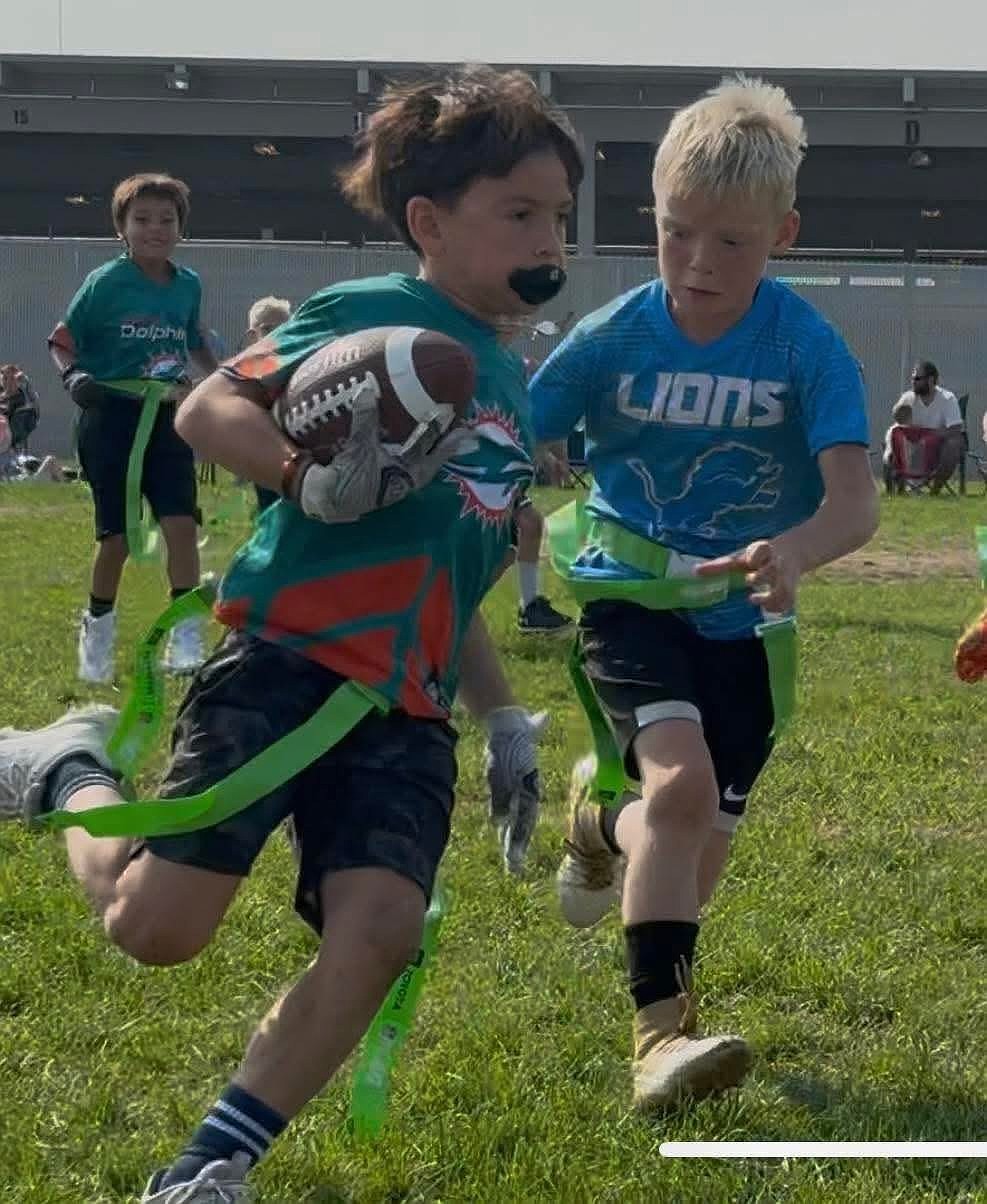 A young player representing the Dolphins rushes with the football while a Lions defender looks to make a stop on the play during last year’s flag football season.
