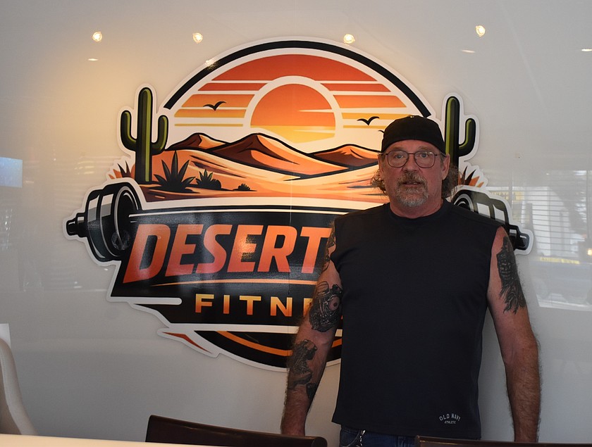 Bryan Boney stands at the front desk in front of the logo for Desert City Fitness. Boney said it was a lot of hard work to get the club started but is already thrilled with the results.