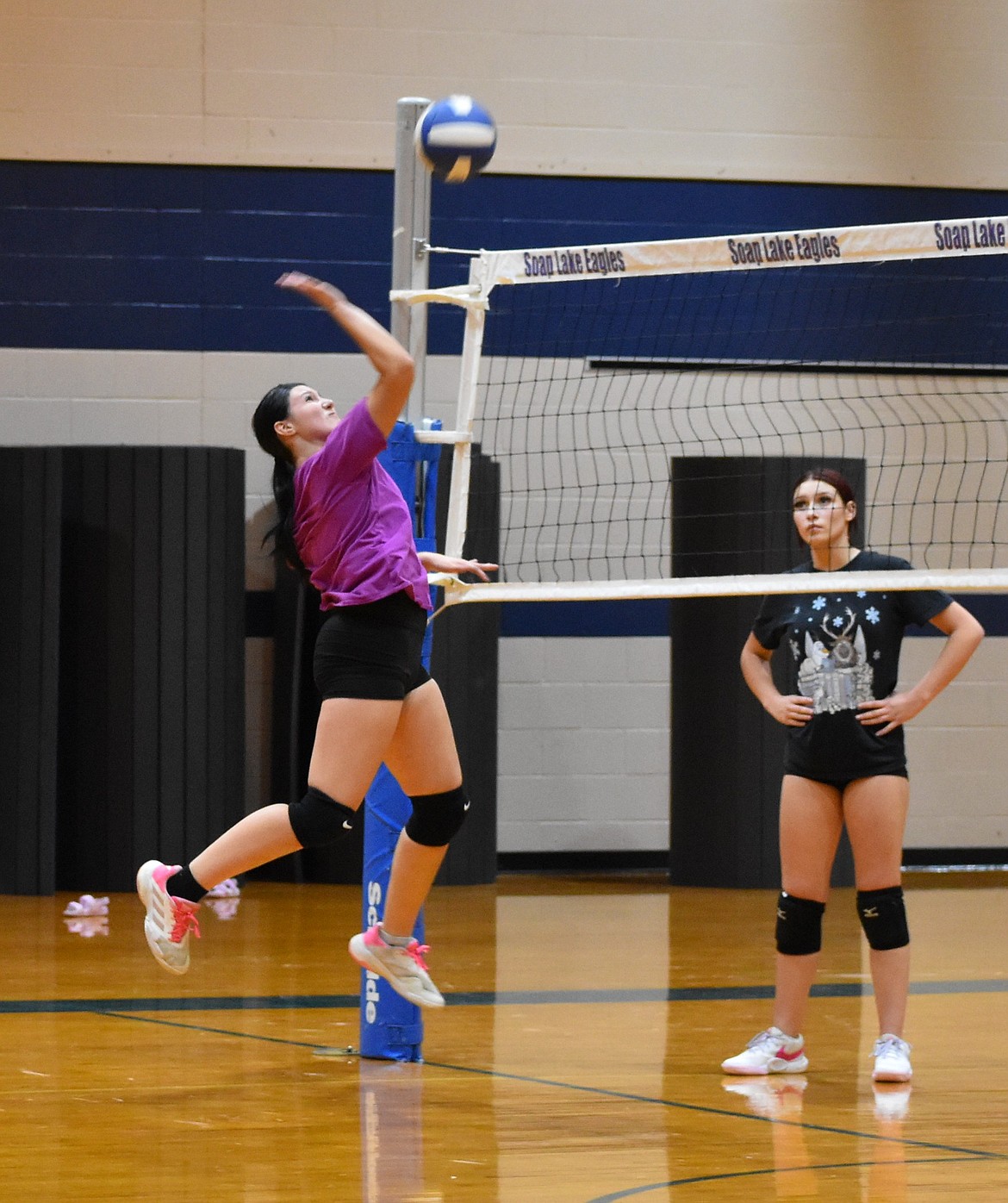 Sanza Gonzalez (pink) leaps up to hit the ball back over the net as her teammate Lily Gonzalez (blue) stands on the other side of the net awaiting her turn to participate in the same exercise.