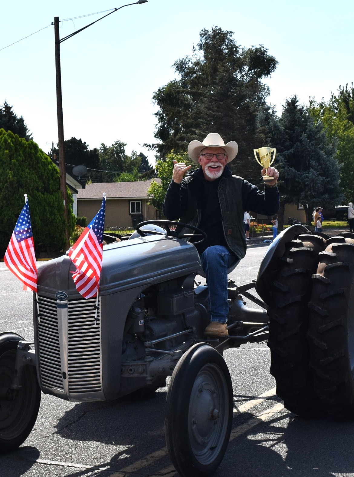 A parade participant proudly displays a first-place trophy for farm equipment while driving his tractor through downtown Warden during Community Days Monday.