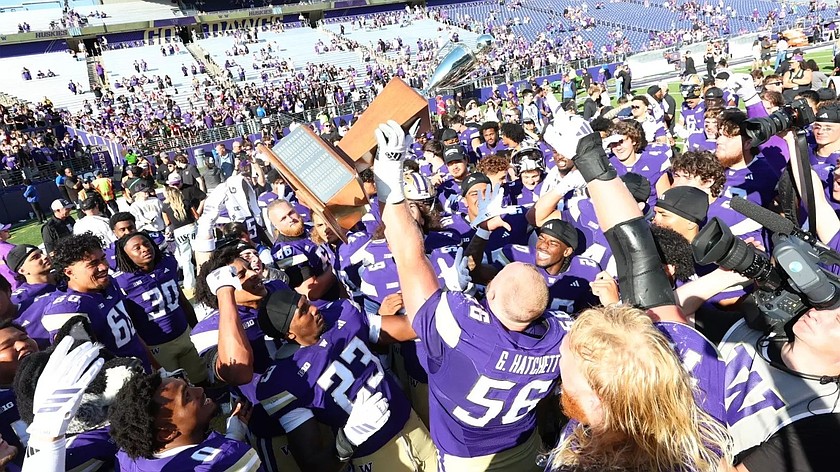 Huskies players gather on the field with Geirean Hatchett holding up the trophy in celebration of the team victory over the Cougars.