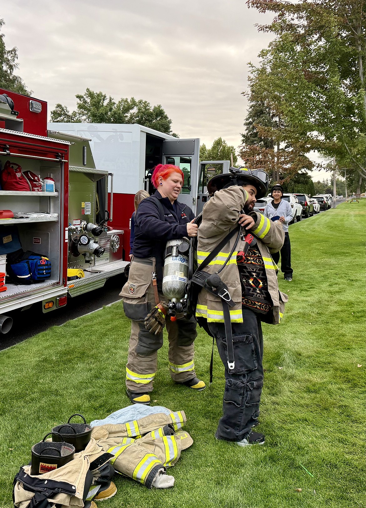 Ephrata Firefighter Emily Grass helps a resident try on gear at National Night Out Tuesday at Lions Park.