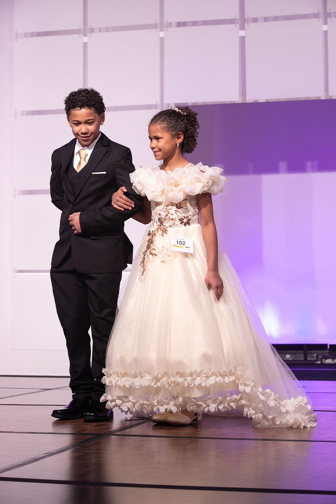 Emberlyn Fields is escorted across the stage by her brother Westley Fields during the formal wear competition at the 2026 National American Miss state pageant in Bellevue, WA. over Labor Day weekend.