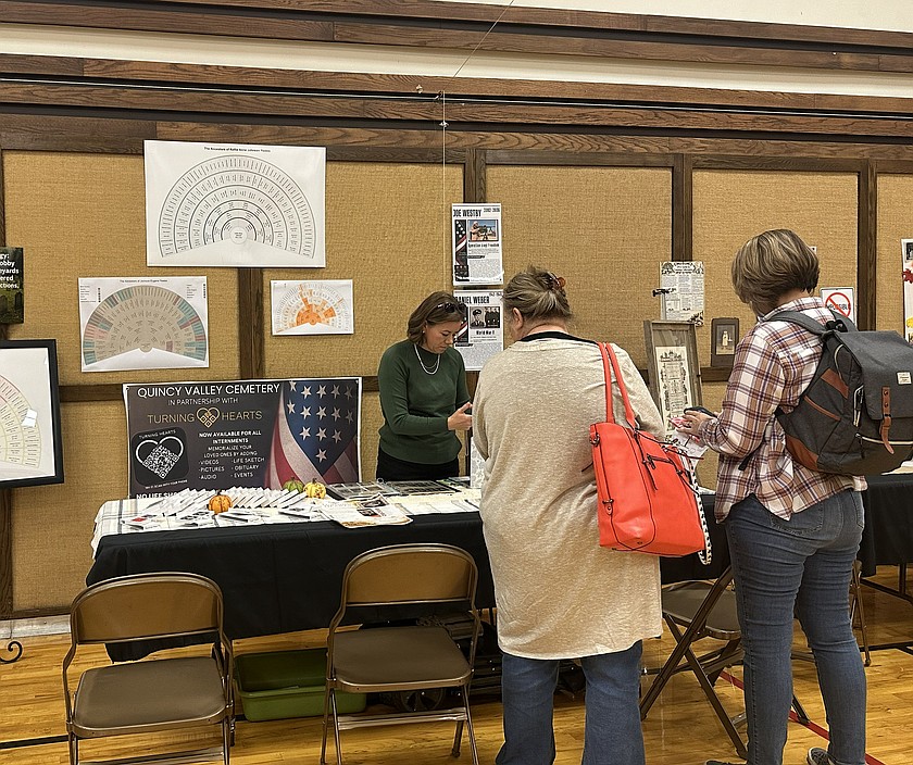 Kellie Yeates, left, shows attendees at the Family History Fair in Ephrata how to use QR codes on a tombstone to learn more about the deceased’s life and family. Behind her are examples of fan charts showing generation after generation of a researcher’s family tree.